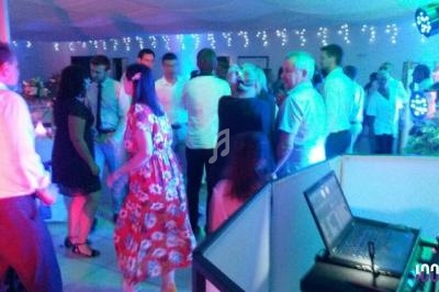 Groupe de personnes dansant et discutant dans une salle éclairée par des lumières colorées, avec une table de DJ au premier…