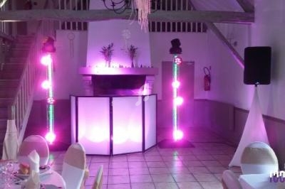 Salle de réception décorée avec des colonnes lumineuses colorées, une table de mixage et des chaises dressées.