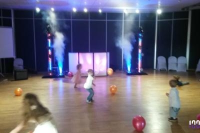 Des enfants jouent avec des ballons colorés dans une salle éclairée par des lumières et de la fumée.