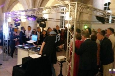 Groupe de personnes rassemblées autour d'une piste de danse avec un DJ mixant sous une structure lumineuse.