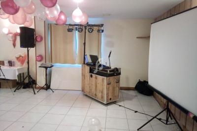Salle décorée avec des ballons roses et blancs, équipée d'un projecteur, d'une table de mixage et d'un micro.