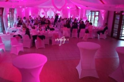 Salle de réception décorée en rose avec des tables dressées et des invités assis lors d'un événement festif.