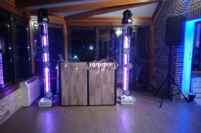 Poste de DJ avec éclairage violet et équipements audio dans une salle aux murs en briques et grandes fenêtres.