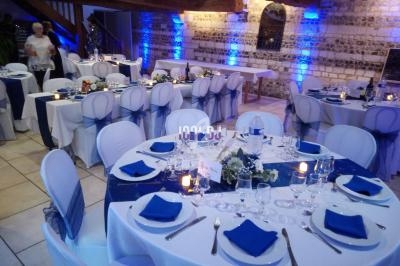 Salle de réception décorée pour un événement, avec tables rondes dressées, nappes blanches et accents bleus.