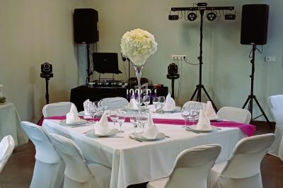 Salle décorée pour un événement avec une table ronde dressée, nappes blanches, centre de table floral et équipement audio.