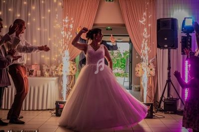 Une mariée danse au centre d'une salle décorée, entourée d'invités et d'effets lumineux festifs.