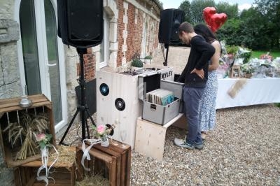 Un couple consulte des vinyles près d'une platine, devant un bâtiment en pierre avec une table décorée en arrière-plan.