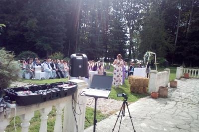 Une femme s'exprime devant un public assis en extérieur, avec une table de mixage et un ordinateur au premier plan.