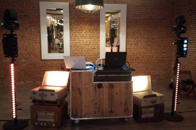 Poste de DJ avec table en bois, équipements audio, éclairages colorés et murs en briques en arrière-plan.