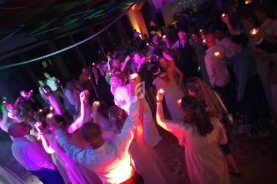Groupe de personnes dansant sous des lumières colorées lors d'une fête, certaines tenant des bougies allumées.