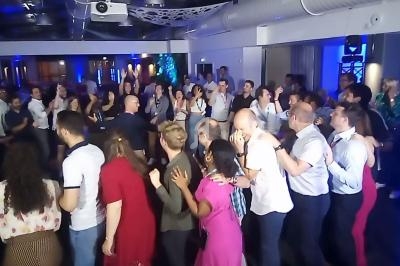 Groupe de personnes dansant en file lors d'un événement festif dans une salle éclairée par des lumières bleues.