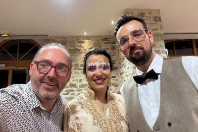 Trois personnes souriantes posent ensemble dans un intérieur avec un mur en pierre et des fenêtres en arrière-plan.