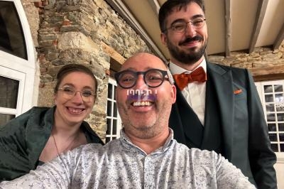 Trois personnes souriantes posent dans une pièce avec des murs en pierre et des poutres apparentes.