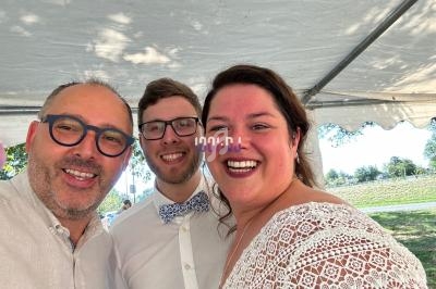 Trois personnes souriantes posent sous une tente blanche par une journée ensoleillée.