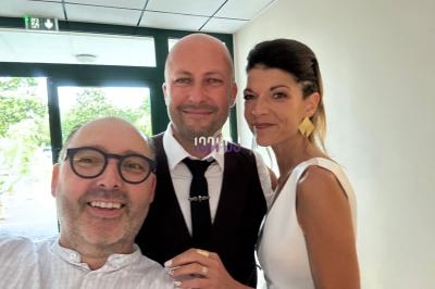 Un homme souriant prend un selfie avec un couple habillé élégamment dans un espace lumineux.