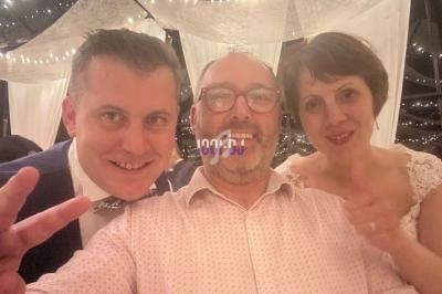 Trois personnes souriantes posent ensemble dans un décor festif avec des guirlandes lumineuses en arrière-plan.