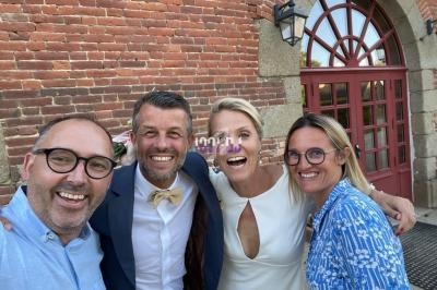 Quatre personnes souriantes posent devant un bâtiment en briques avec une grande porte vitrée en arche.
