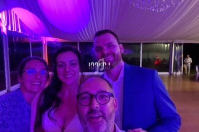 Quatre personnes souriantes posent sous un éclairage violet dans une salle avec un plafond drapé et un lustre.