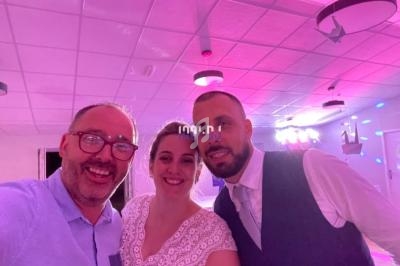 Trois personnes souriantes posent ensemble dans une salle éclairée par des lumières roses et violettes.