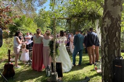 Un mariage en plein air avec des invités rassemblés autour des mariés sous une arche décorée, dans un jardin verdoyant.
