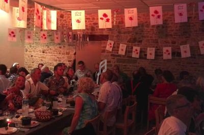 Des personnes assises à des tables dans une salle décorée de guirlandes avec des motifs de coquelicots.