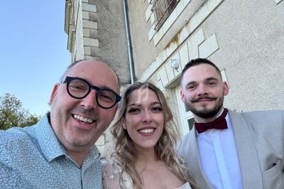 Trois personnes souriantes posant devant un bâtiment en pierre sous un ciel dégagé.