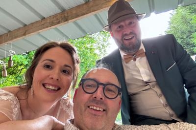 Trois personnes souriantes posent sous un abri en bois, avec un arrière-plan de verdure.