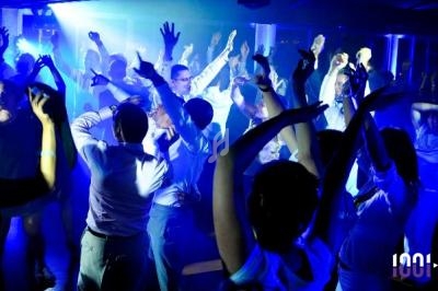 Des personnes dansent sous des lumières colorées dans une ambiance festive en boîte de nuit ou lors d'une soirée.