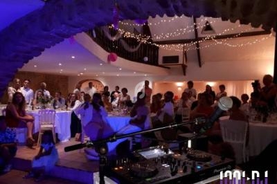 Salle de réception décorée avec des guirlandes lumineuses, des invités assis et une table de mixage au premier plan.