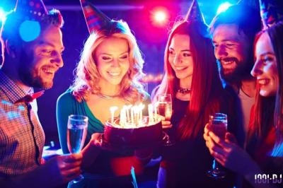 Des amis souriants célèbrent un anniversaire avec un gâteau illuminé par des bougies et des coupes de champagne.