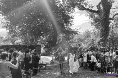 Un couple marche main dans la main sous un rayon de soleil, entouré d'invités lors d'une cérémonie en plein air.