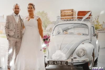 Un couple en tenue de mariage pose devant une voiture ancienne décorée pour l'occasion.