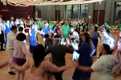 Des personnes dansent en cercle dans une salle éclairée, décorée de rubans suspendus au plafond.