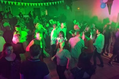 Des personnes dansent dans une salle éclairée par des lumières colorées, décorée de guirlandes et de ballons.