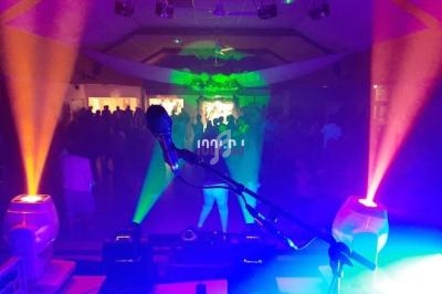 Vue depuis une table de mixage avec micro et éclairages colorés, face à une salle remplie de personnes dansant.