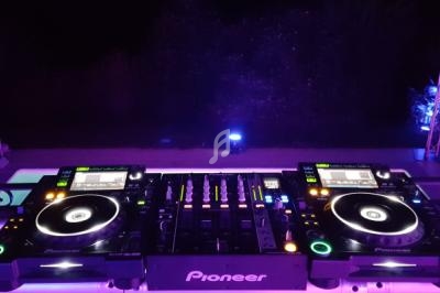 Deux platines DJ et une table de mixage éclairées par des lumières violettes dans un environnement sombre.