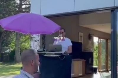 Un homme mixe de la musique sur une terrasse extérieure, près d'une maison avec de grandes baies vitrées ouvertes.