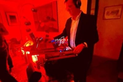Un DJ mixe de la musique dans une pièce éclairée par une lumière rouge, entouré d'équipements audio.