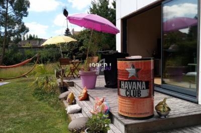 Terrasse en bois avec des plantes en pot, un baril décoratif, un parasol rose et un jardin en arrière-plan.