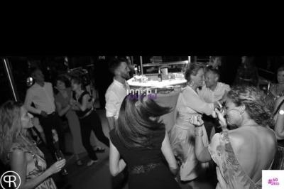 Des personnes dansent et discutent dans une ambiance festive en noir et blanc, autour d'une piste et d'un bar.