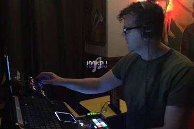 Un DJ mixant de la musique sur une console éclairée, dans une pièce faiblement éclairée avec des tableaux en arrière-plan.