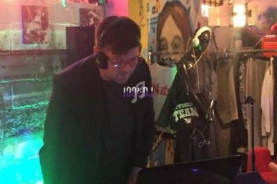 Un DJ mixe de la musique sur une table de mixage dans un espace coloré et décoré de graffitis et d'objets lumineux.