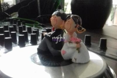 Figurines de mariés en tenue de cérémonie posées sur une platine de mixage dans un décor intérieur.