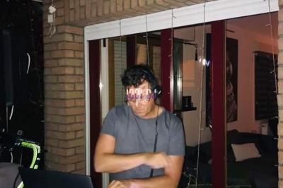 Un DJ mixe de la musique sur un contrôleur devant un ordinateur portable dans un espace intérieur faiblement éclairé.