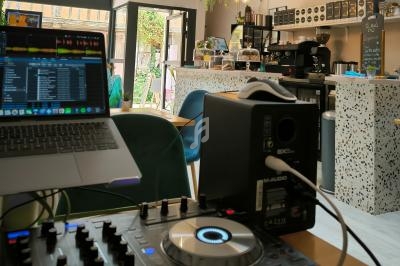 Poste de DJ avec contrôleur et ordinateur portable dans un café moderne, décoré de plantes et éclairé naturellement.