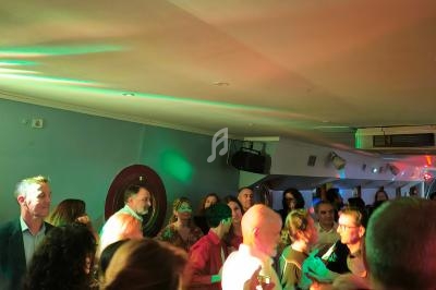 Des personnes dansent et discutent dans une salle éclairée par des lumières colorées lors d'un événement festif.