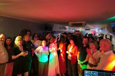 Groupe de personnes debout dans une salle éclairée par des lumières colorées, semblant participer à un événement festif.
