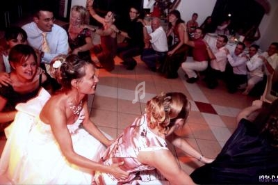 Des invités dansent en ligne lors d'une fête, avec une mariée en robe blanche au premier plan.