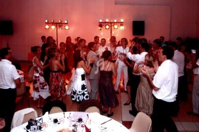 Des invités dansent et discutent dans une salle de réception éclairée, décorée pour un événement festif.