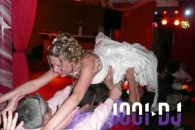 Une mariée en robe blanche est portée en l'air par des invités lors d'une fête avec éclairages colorés.